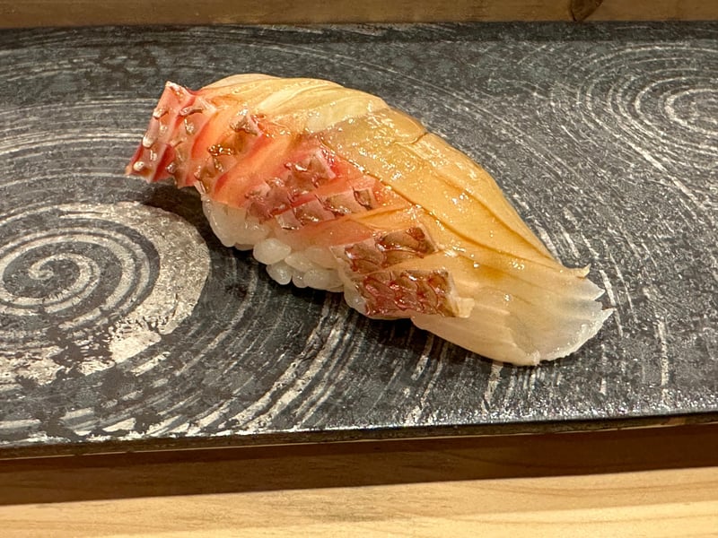 波紋の黒い板皿にのった真鯛の握り。皮目に細かく包丁が入っている