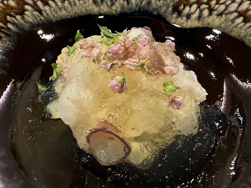 黒い鉢の水蛸に透明な出汁ジュレがかかり、穂紫蘇が添えられている