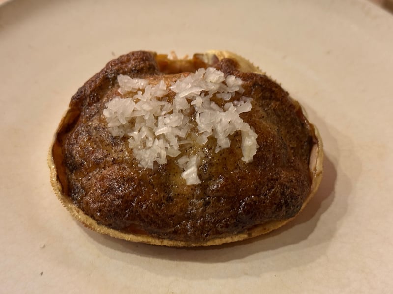 甲羅ごと焼いた蟹味噌。表面に焼き色がつき、上に白いみじん切りを散らして