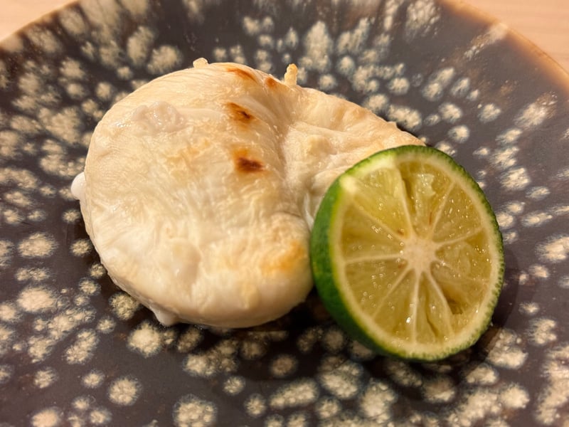 白い斑紋の鉢に、焼き目をつけたトラフグの白子と半割の柑橘