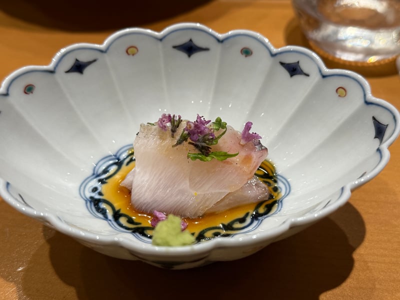 たれを敷いた輪花の染付鉢に、皮を炙った目鯛の切り身。穂紫蘇の花とわさびを添えて