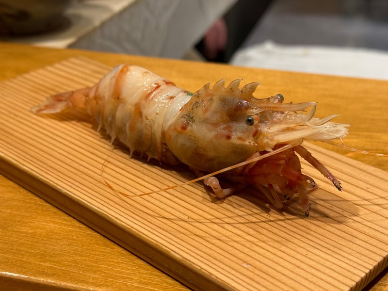 板の上に置かれた生の海老一尾。棘のある頭と長いひげ