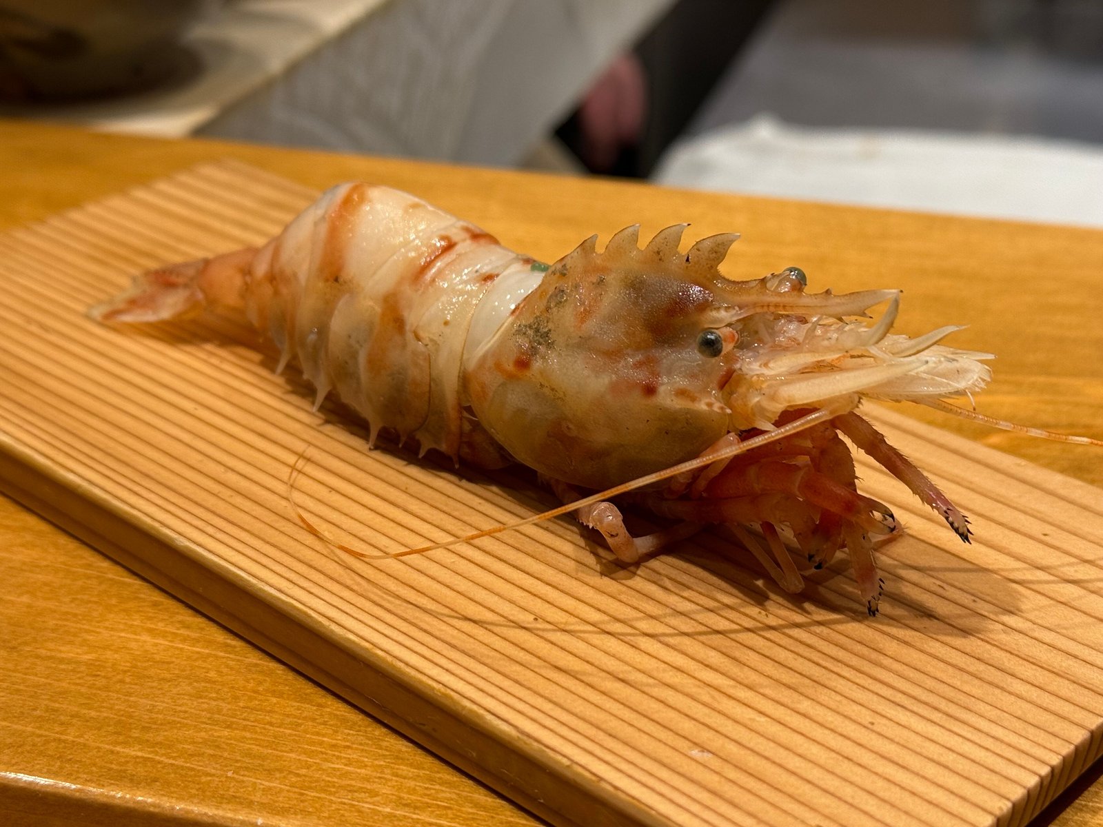 板の上に置かれた生の海老一尾。棘のある頭と長いひげ