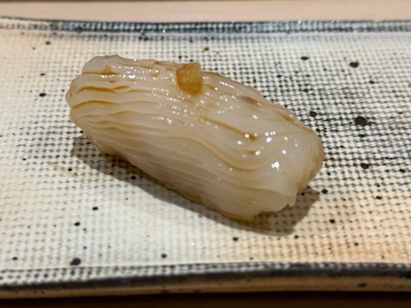 黒点の入った角皿に載ったアオリイカの握り、上に少量のわさび