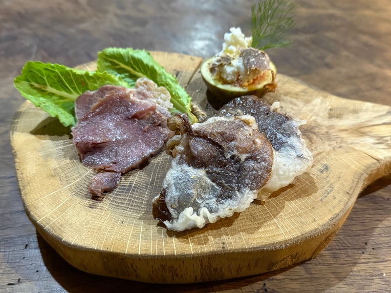 木の板にのった三品。薄桃色のハム、衣をつけて揚げた椎茸、半分に切ったいちじくに白いヤギのチーズ