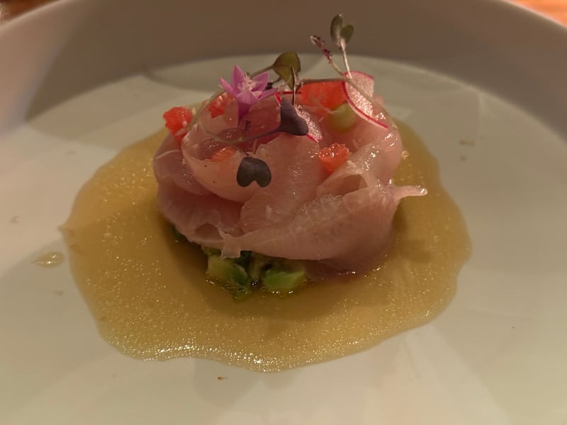 白い皿に薄く引いたドレッシング。その上に丸く盛ったハマチとアボカド、花と芽をのせて