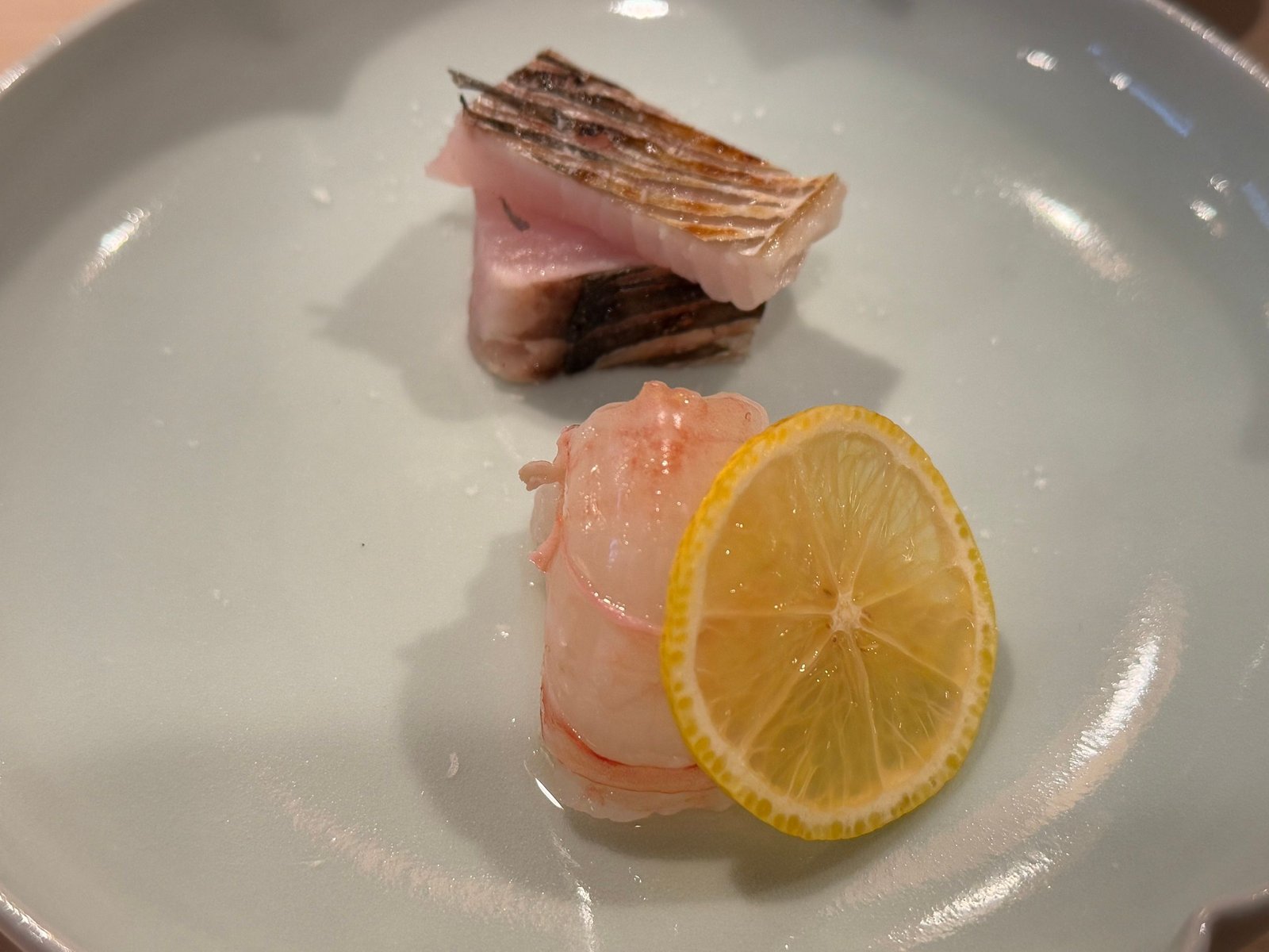 白い皿に、皮を炙った岩船のさわらと、レモンを添えた佐渡のボタンエビ