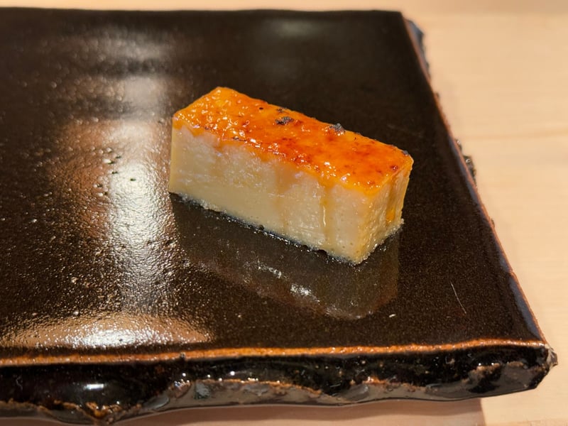 黒い角皿に、表面を焦がした棒状の卵