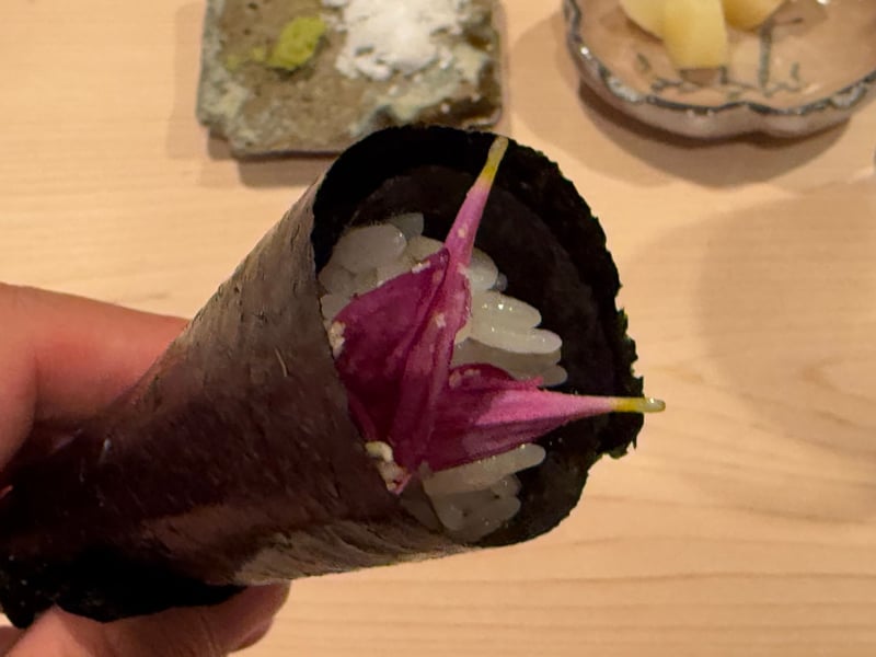 手に持った手巻き。飯の上に紫の菊の花びらを二枚