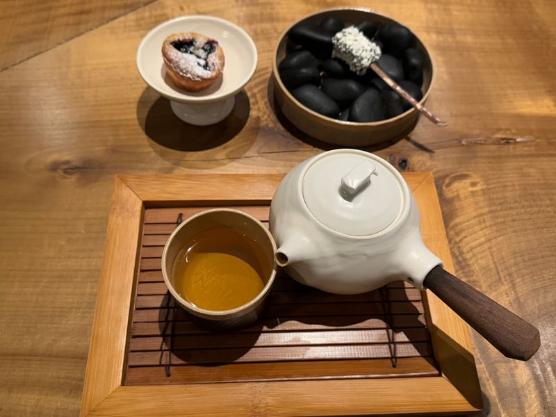 白い急須と茶、ブルーベリーのタルト、黒い石の上に串を刺した白い一口