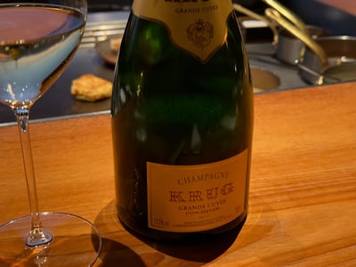 クリュッグ グランド・キュヴェ 171エディションのボトルとグラス。奥の鉄板のカウンターにチーズのチュイールが一枚