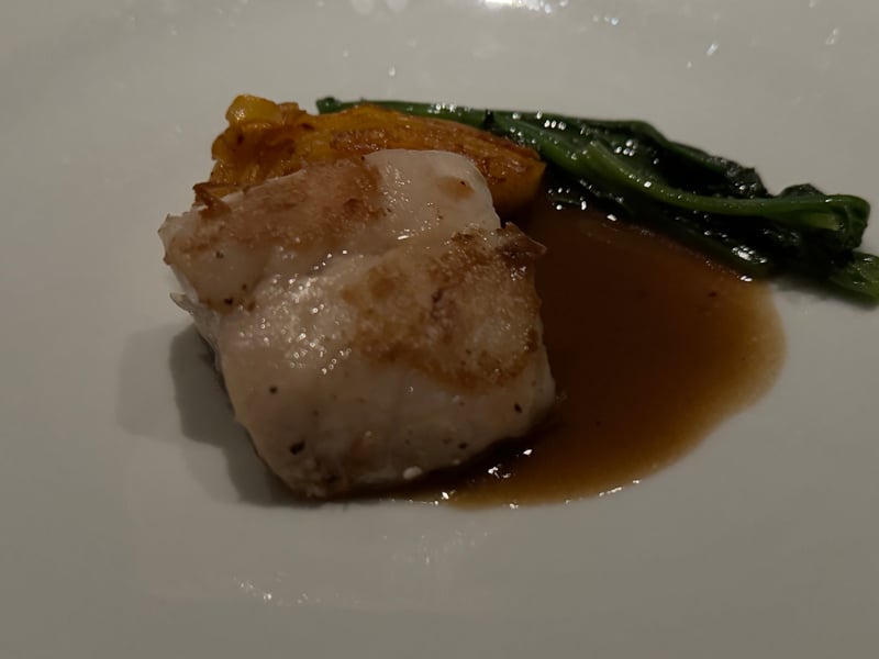 白い皿に皮目を焼いたマハタの切り身、焼いた根セロリとほうれん草、茶色いソース