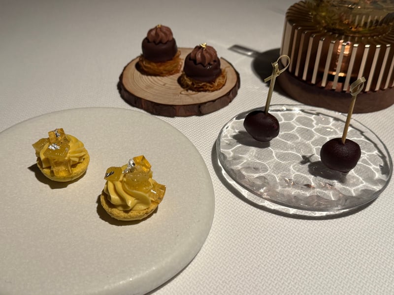 3つの器に分けた小菓子。黄色いクリームのマカロン、細い衣の上のチョコレート、串に刺した丸いチョコレート