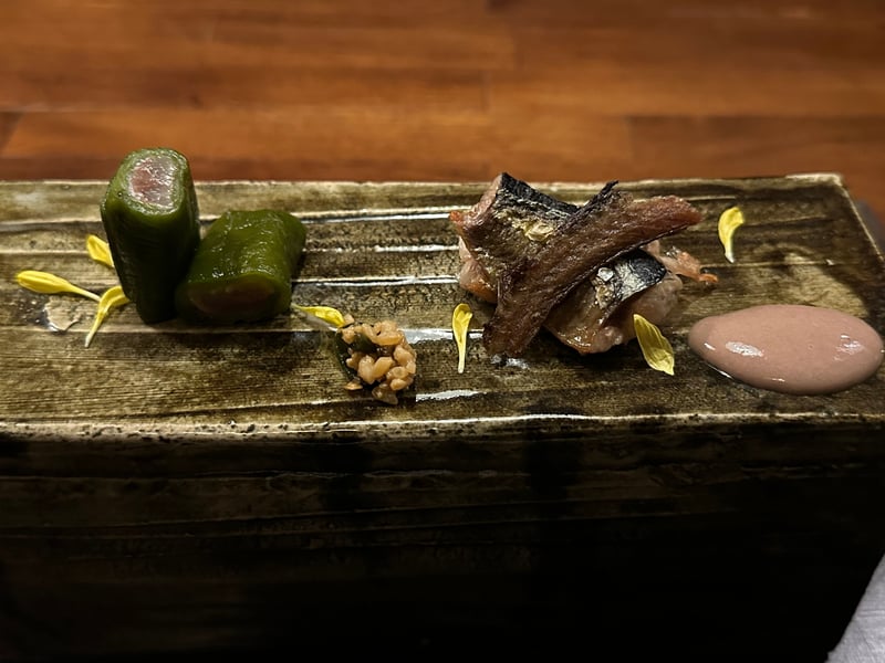 灰釉の長皿。詰め物をした青い唐辛子と焼いた秋刀魚、褐色のペースト、菊の花びら