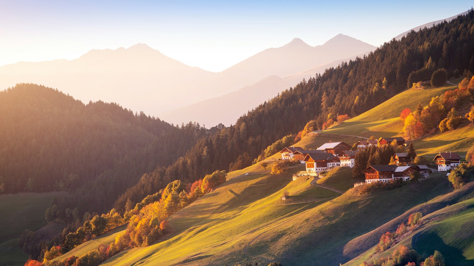 Maisons sur des coteaux verdoyants au coucher du soleil, montagnes en arrière-plan