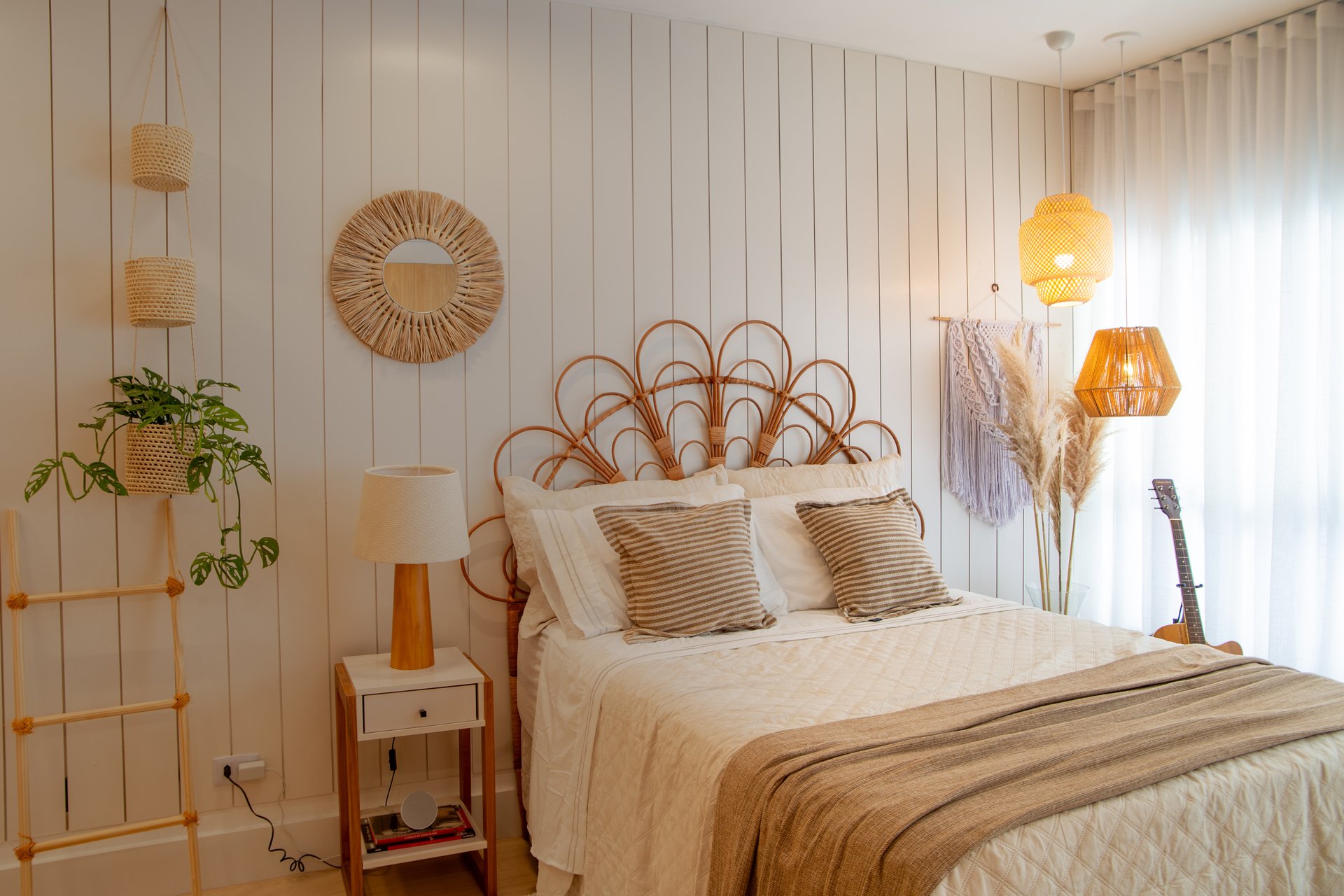 Foto de um comodo com a cortina iluminada de fundo, da esquerda pra direita: um abajour, uma cama e um violão