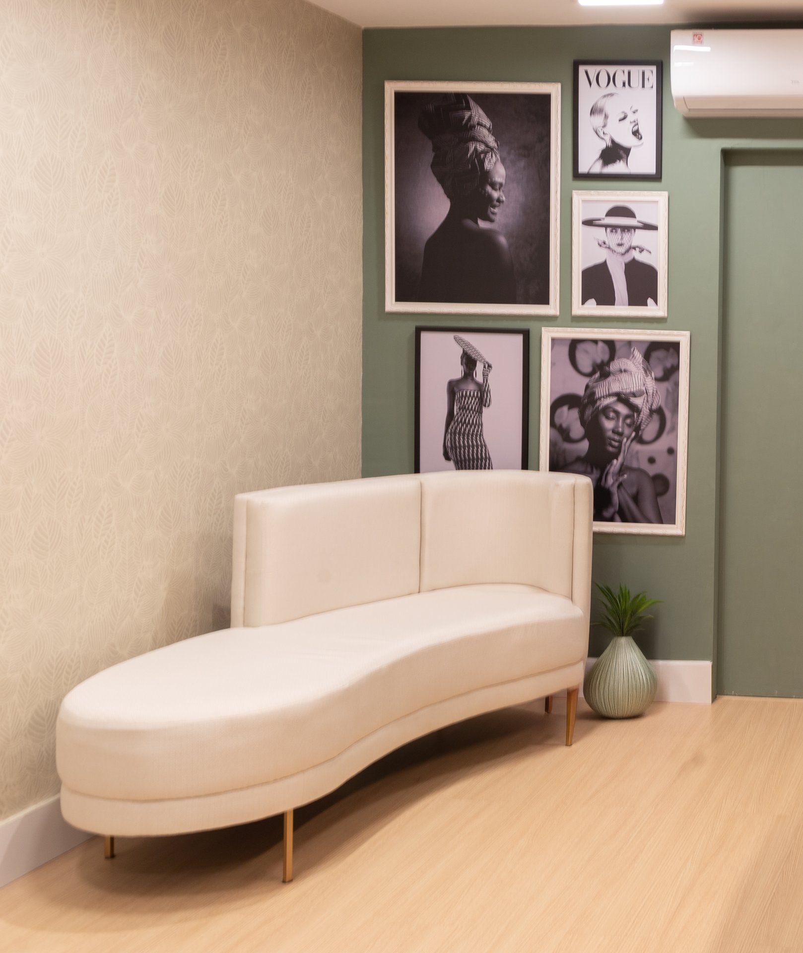 Um canto com um sofá e vários quadros na parede verde musgo
