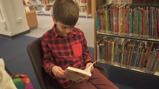 boy sitting in a chair, reading a book