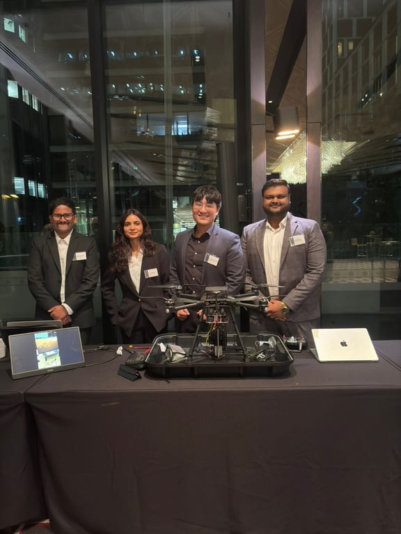 Four teammates at a demo table with a quadcopter, monitor, and controls