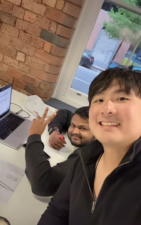Two teammates smiling in an office with brick wall and window light