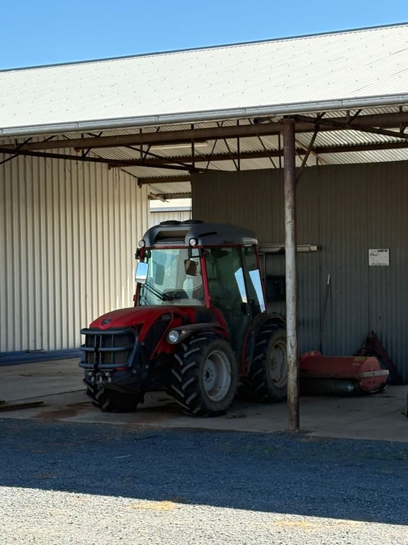 Red tractor parked under a corrugated farm shed on concrete