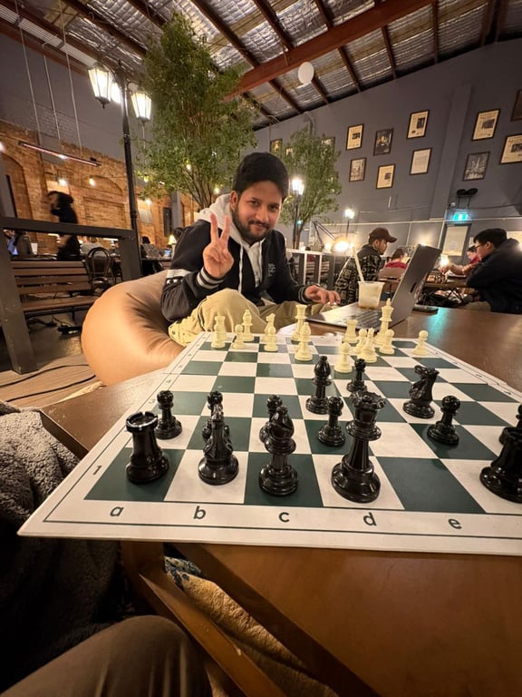 A man posing infront of a chess board, with people working on computers in the background