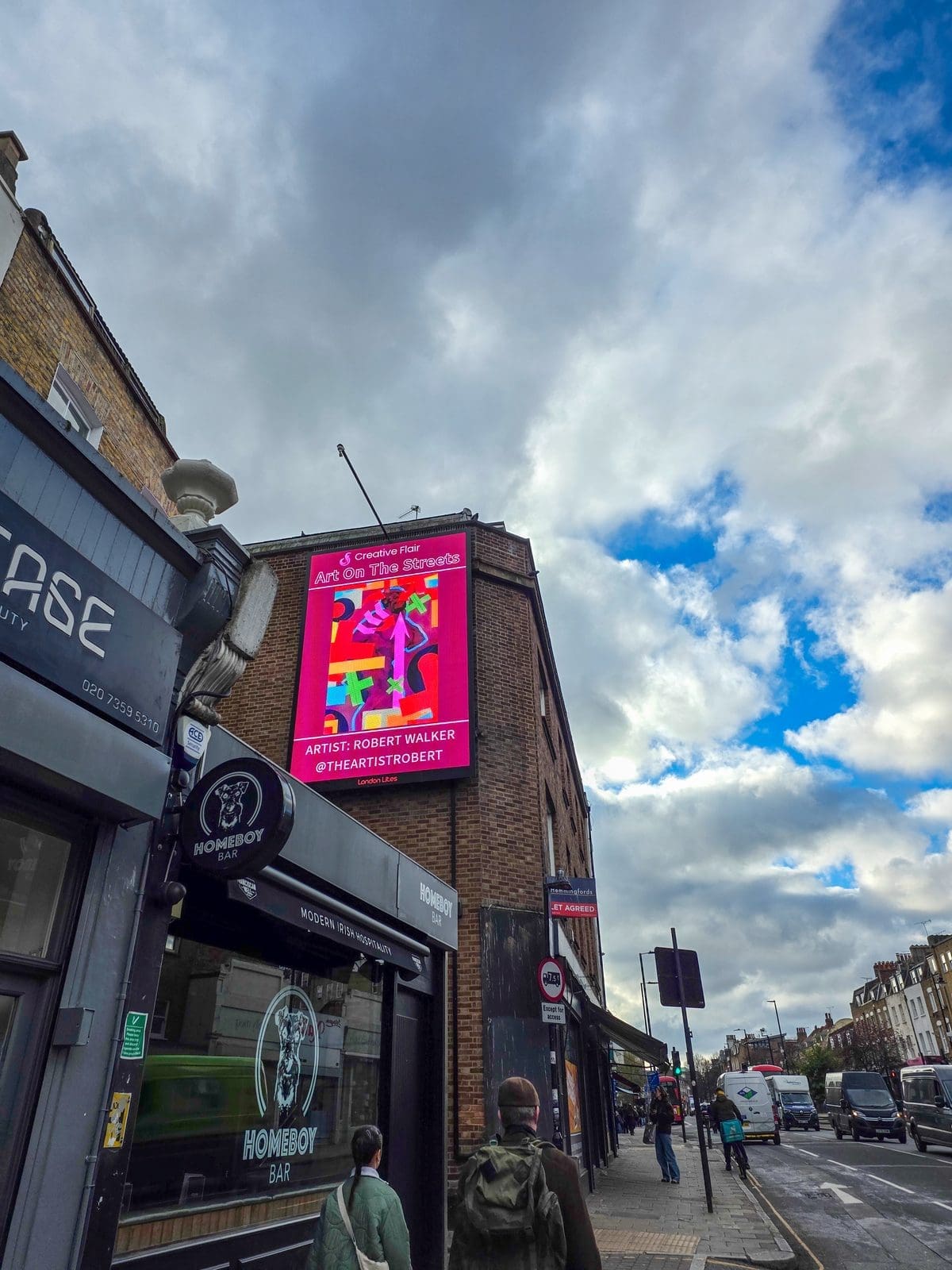 Robert Walker standing in front of his artwork featured on the Art On The Streets London Art Fair billboard - artist billboard showcase on Essex Road digital screen