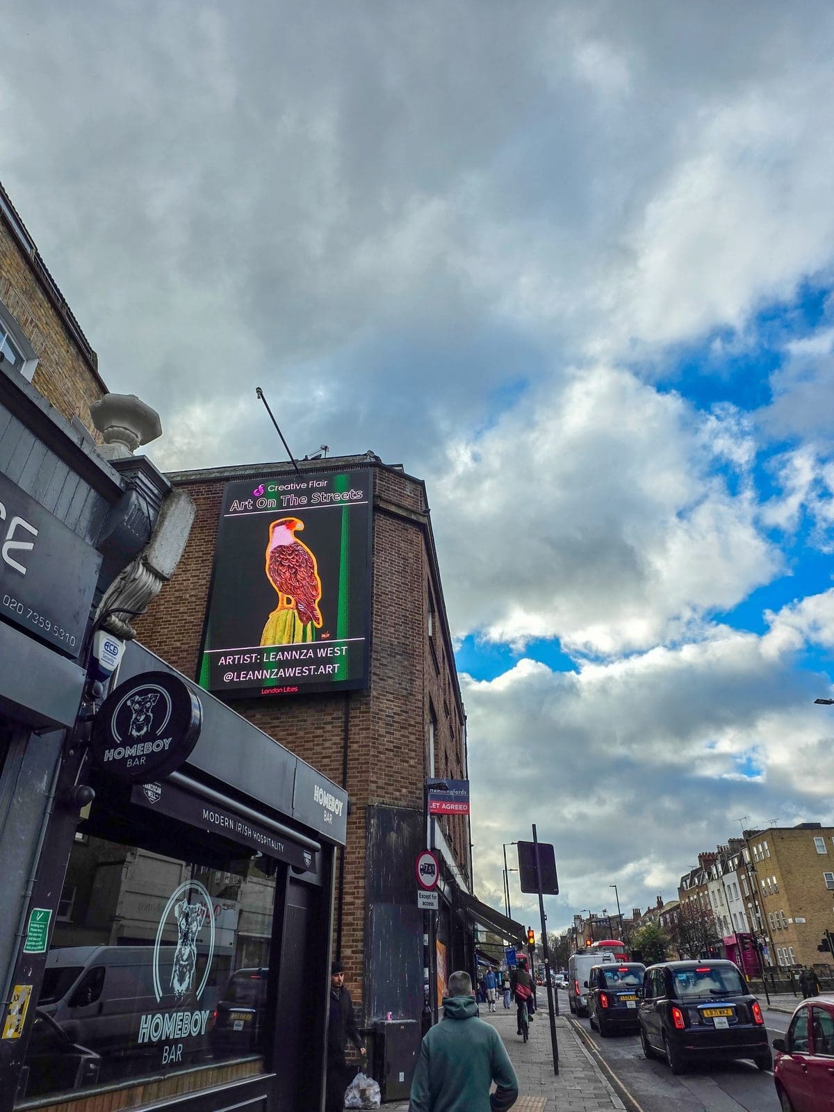 Leannza West posing with her featured artwork on the Art On The Streets London Art Fair billboard - artist billboard exhibition at Essex Road during art fair opening day