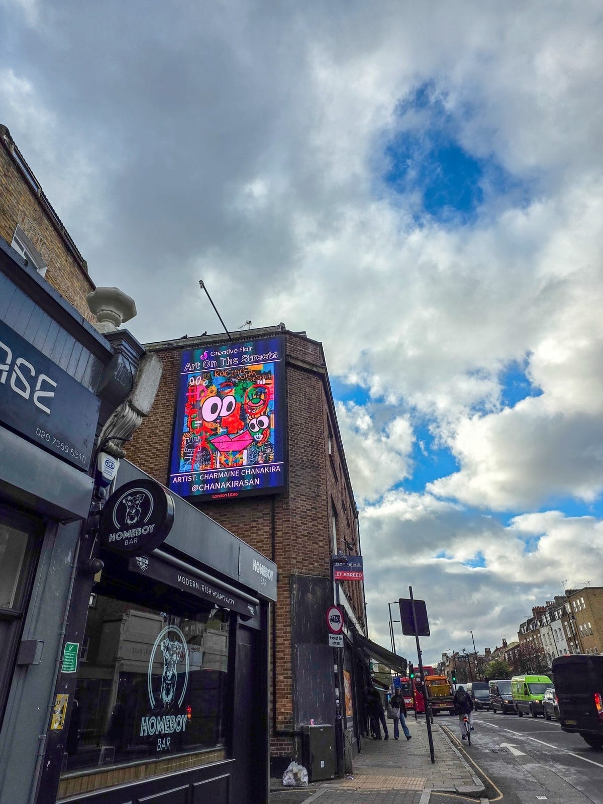 Charmaine Chanakira standing in front of billboard artwork displayed during London Art Fair - Art On The Streets artist billboard exhibition with gallery visitors