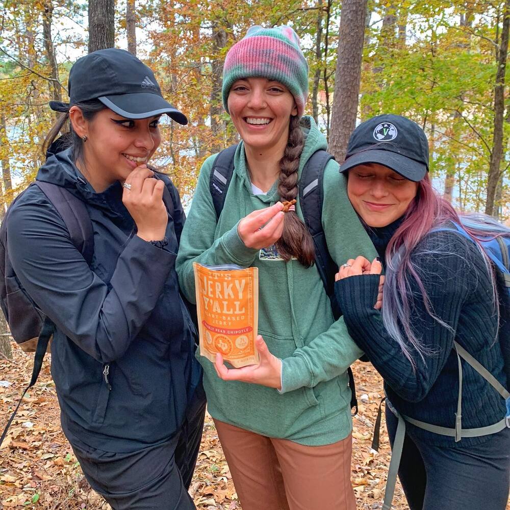 Three girls eating plant-based jerky while camping