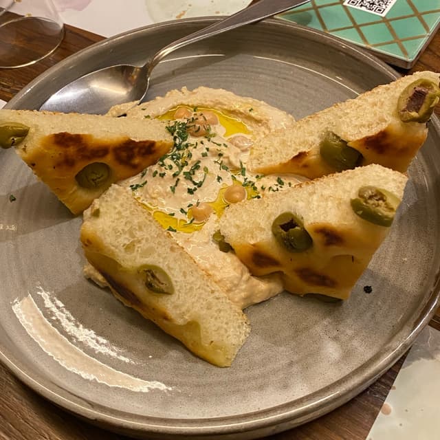Foto do prato “Hummus Di ceci con focaccia alle olive e olio evo”