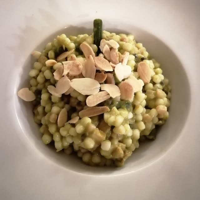 Foto do prato “Fregula risottata, crema di fagiolini, capperi di lipari, fagiolini croccanti, mandorle tostate e tofu affumicato alla paprika”