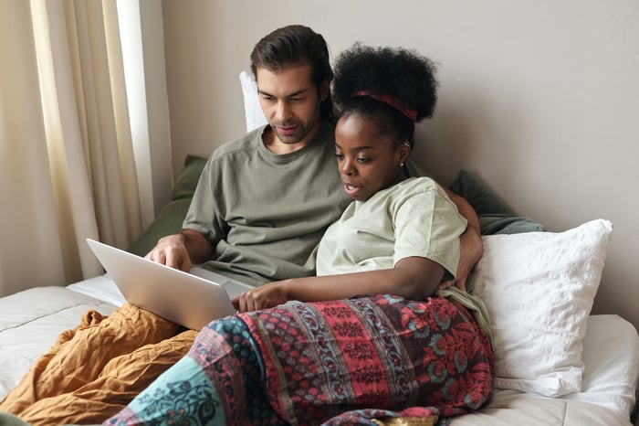 couple sitting on a bed discussing over a laptop