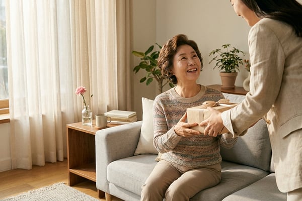 어버이날 엄마에게 선물 상자를 전하는 딸의 따뜻한 거실 장면, 60대 한국 엄마와 카네이션