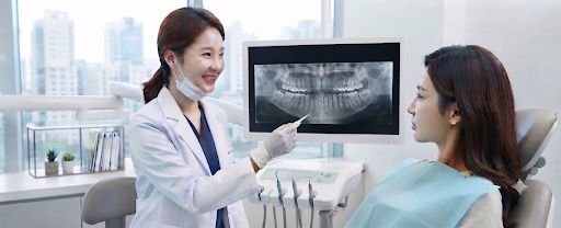 치과의사가 치과 진료실에서 파노라마 엑스레이 화면을 가리키며 환자에게 치아 상태를 설명하고 있는 모습