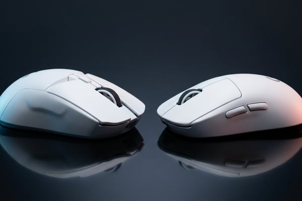 어두운 반사면 위에 놓인 두 개의 흰색 무선 게이밍 마우스 — 왼쪽은 약간 크고 각진 지슈스, 오른쪽은 컴팩트한 지슈라 2c