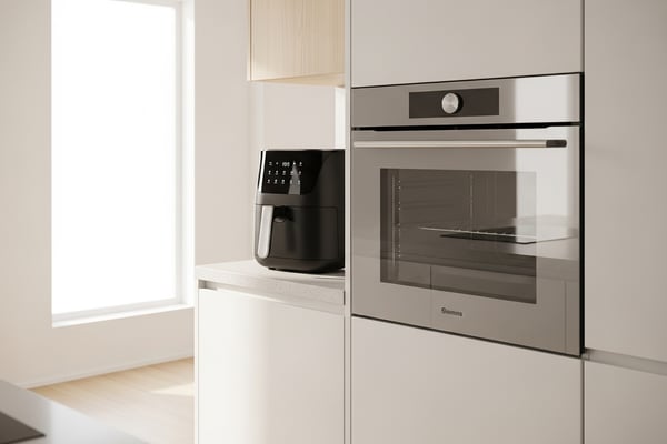 모던 한국 주방 조리대 위에 검정 에어프라이어와 스테인리스 빌트인 오븐이 나란히 놓인 모습, 미니멀 화이트 인테리어와 자연광