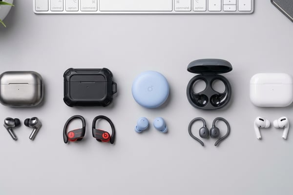 다양한 스타일의 무선 이어폰 5종과 충전 케이스를 라이트 그레이 책상 위에 정갈하게 배치한 플랫레이 사진