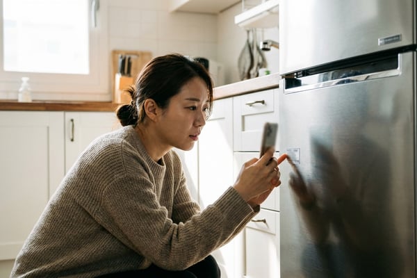 냉장고 옆면의 모델명 스티커를 스마트폰으로 확인하는 여성