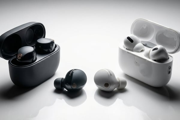 소니 WF-1000XM5와 애플 에어팟 프로 2가 흰색 표면 위에서 마주보고 놓인 프리미엄 오디오 제품 사진, 양쪽에서 비추는 드라마틱한 조명