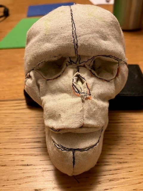 Skully grins at you! A small handmade skull stuffed with scraps made in a pale beige calico fabric faces the viewer.