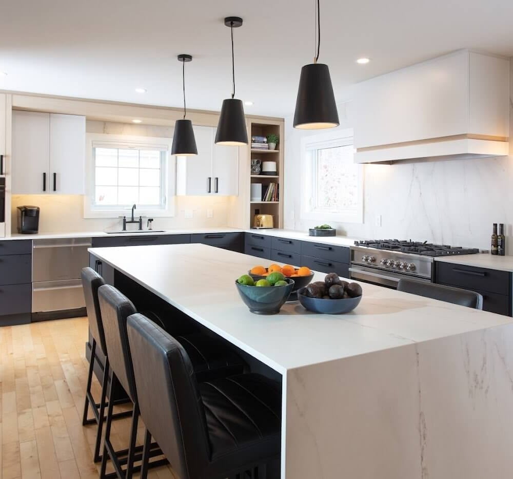 Modern kitchen with dark lower cabinets, white upper cabinets, a large marble-look island and black pendant lights.