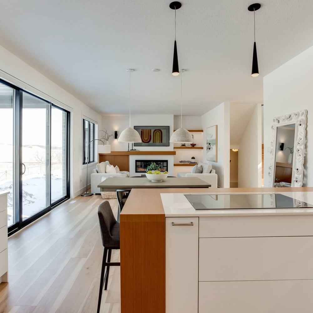1T9hdl34 Modern kitchen with white cabinetry, a central island, and pendant lighting, featuring an open layout to a living area with large windows.