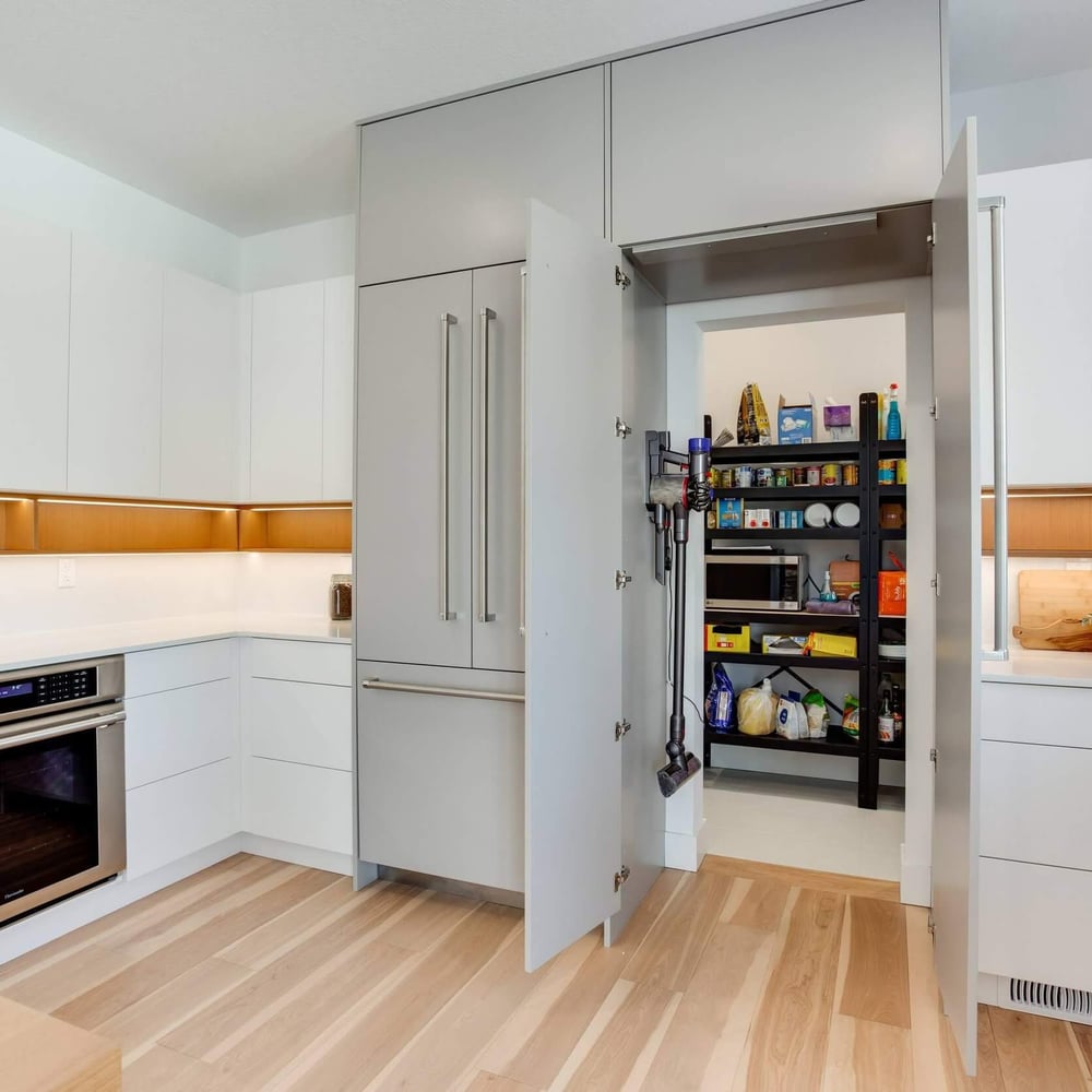 OP_xMx-8 Modern kitchen with sleek cabinetry, an open pantry, and a built-in oven, featuring light wood flooring and minimalist design elements.