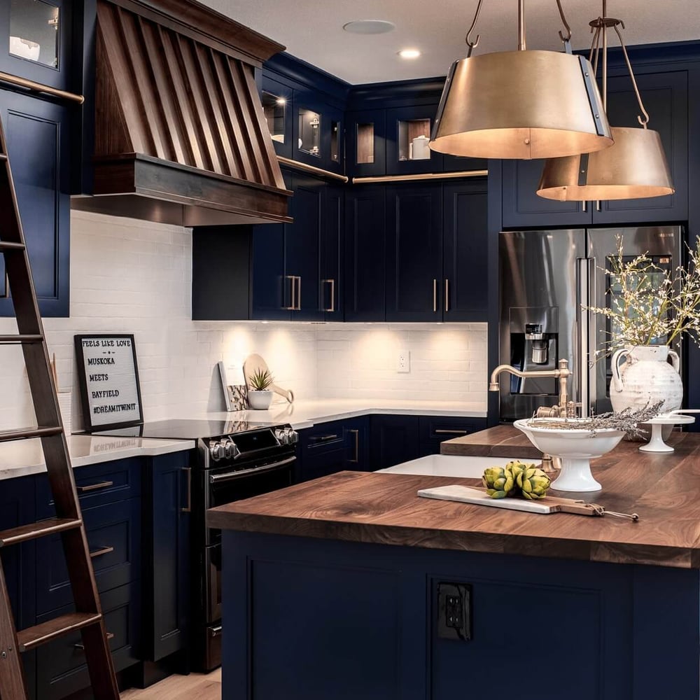 Modern kitchen with navy blue cabinetry, a wooden island, pendant lighting, and a ladder against the wall.