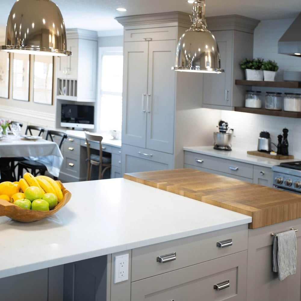 Project_Kitchens_Eastbridge Modern kitchen with a wooden bowl of fruits on a countertop, stainless steel appliances, and stylish pendant lighting.