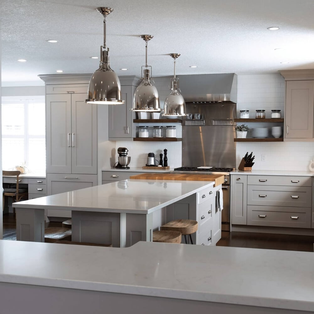 Project_Kitchens_Eastbridge2 Modern kitchen with gray cabinetry, white countertops, and pendant lighting, featuring an island and stainless steel appliances.