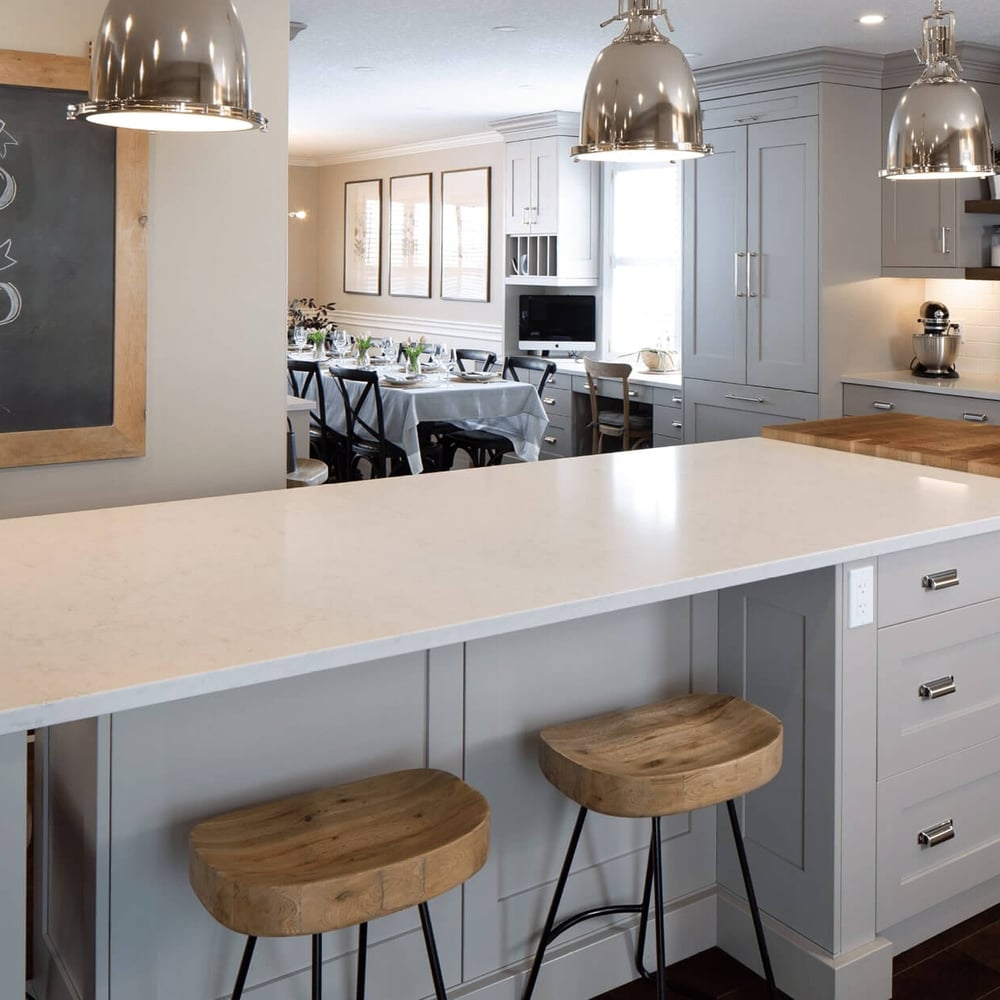 Project_Kitchens_Eastbridge4 Modern kitchen with a large white countertop island, wooden bar stools, and stainless steel appliances.