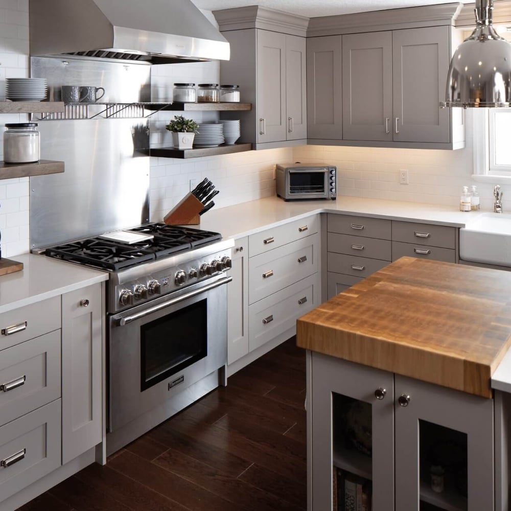 Project_Kitchens_Eastbridge_MAIN Modern kitchen with gray cabinetry, stainless steel appliances, and a large wooden island with a sink.