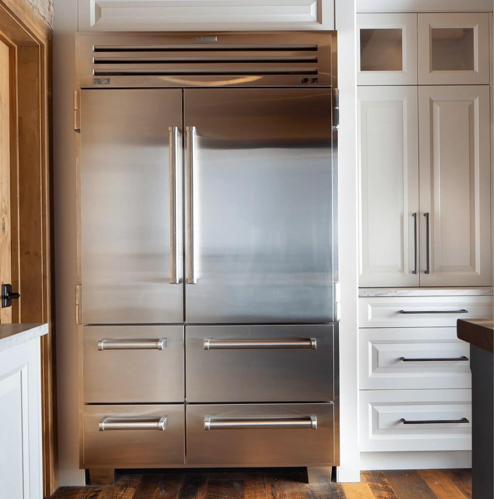 Project_Kitchens_Fruit+Ridge10 Stainless steel refrigerator with double doors and a sleek design, positioned next to white cabinetry in a modern kitchen.